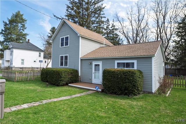 rear view of property with a shingled roof, fence, and a lawn