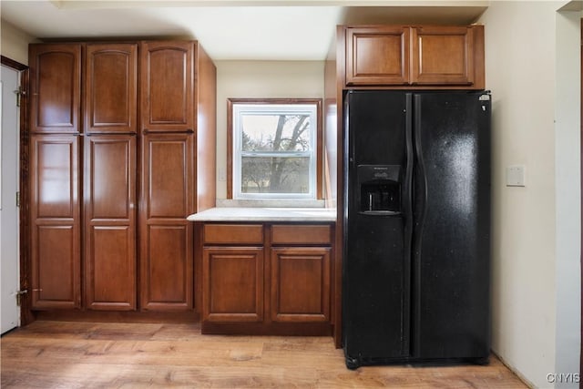 kitchen with light wood finished floors, light countertops, brown cabinetry, and black fridge with ice dispenser
