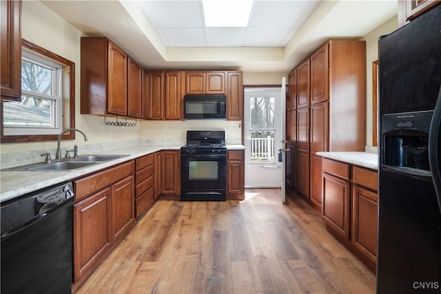 kitchen with a wealth of natural light, a tray ceiling, a sink, and black appliances
