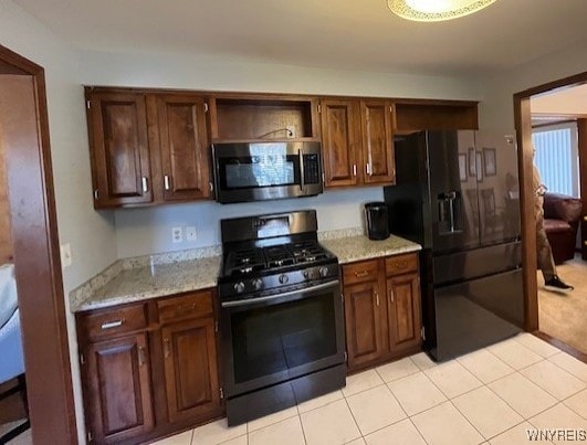 kitchen featuring light tile patterned floors, stainless steel microwave, light stone counters, gas stove, and black refrigerator with ice dispenser