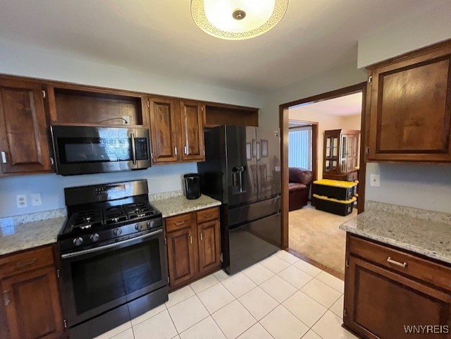 kitchen featuring light tile patterned floors, black appliances, light stone countertops, and light colored carpet