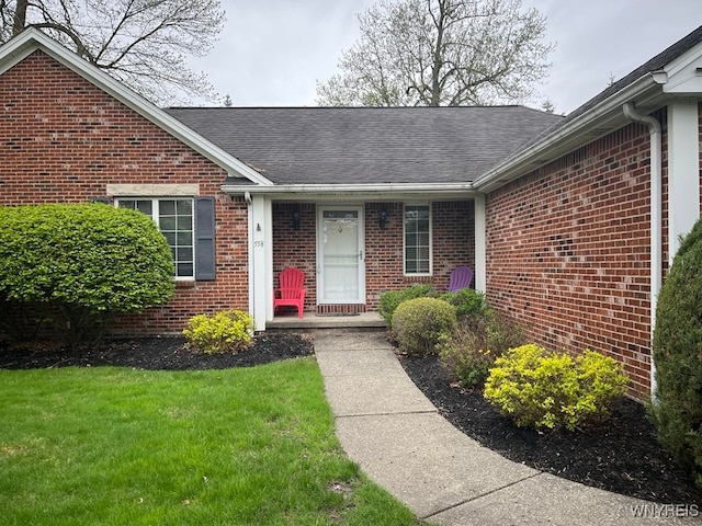entrance to property with brick siding, roof with shingles, and a lawn