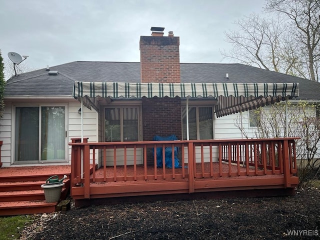 back of property with a chimney, a wooden deck, and roof with shingles