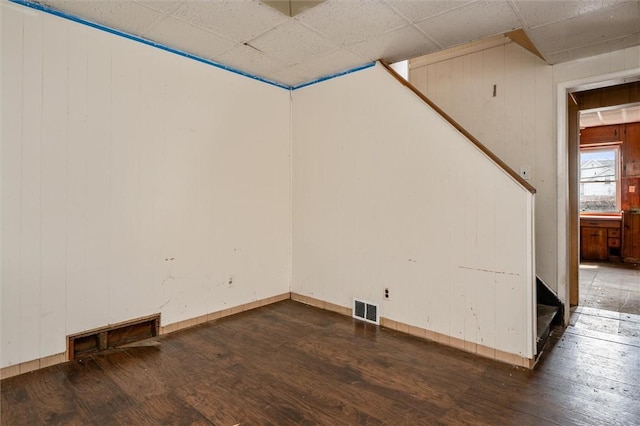 empty room featuring a paneled ceiling, wood-type flooring, visible vents, and stairway