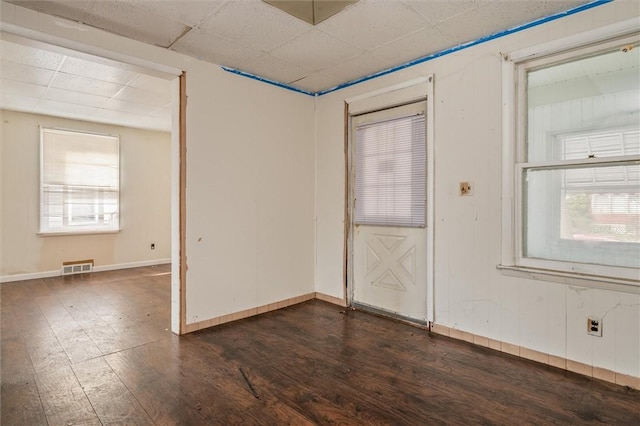 unfurnished room featuring dark wood-type flooring, visible vents, baseboards, and a paneled ceiling
