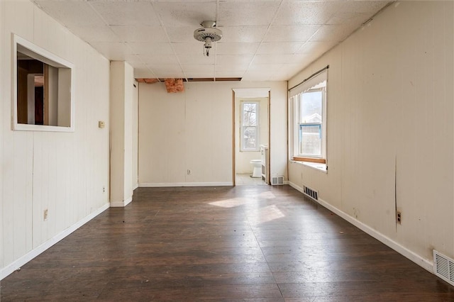 empty room with dark wood-style floors, baseboards, and visible vents