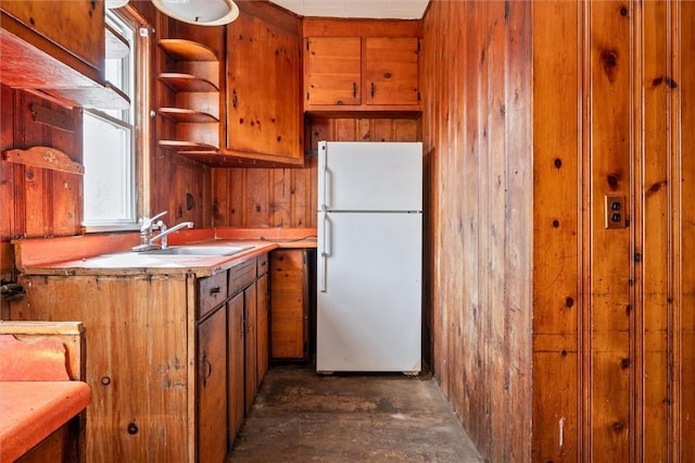 kitchen with freestanding refrigerator, brown cabinetry, open shelves, a sink, and wooden walls