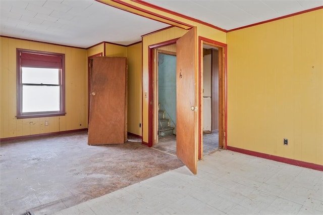 spare room featuring wood walls, stairway, crown molding, and light floors