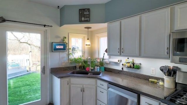 kitchen with white cabinets, dark countertops, a sink, stainless steel appliances, and decorative light fixtures