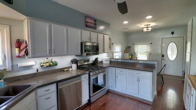 kitchen with white cabinets, dark wood-style flooring, dark countertops, appliances with stainless steel finishes, and a peninsula