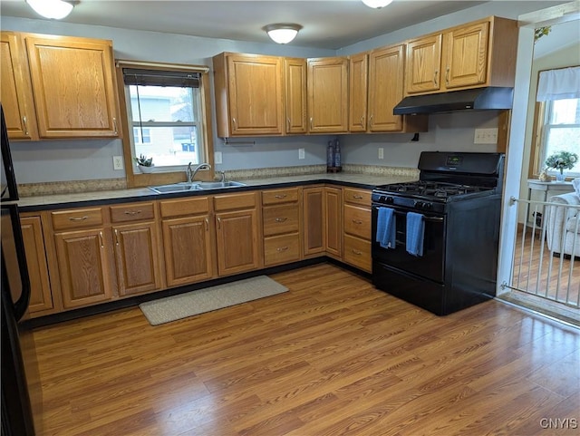 kitchen with a sink, a wealth of natural light, light wood-type flooring, under cabinet range hood, and black range with gas stovetop
