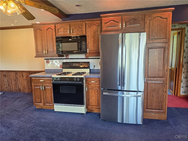 kitchen featuring wallpapered walls, gas stove, black microwave, freestanding refrigerator, and wainscoting