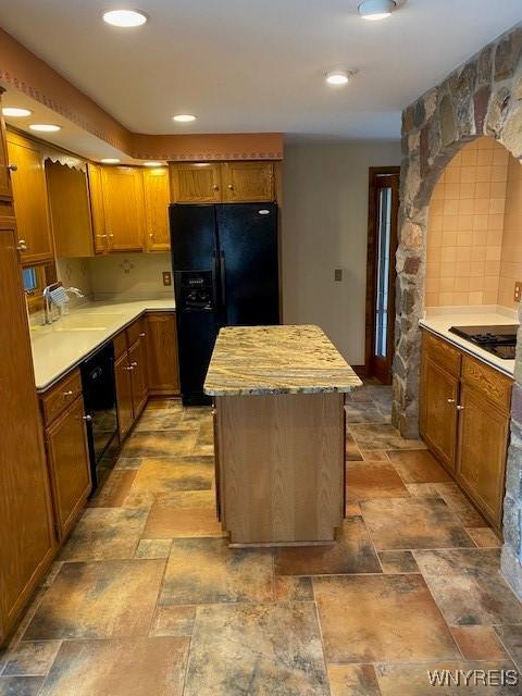 kitchen featuring stone finish flooring, black appliances, a kitchen island, a sink, and light countertops