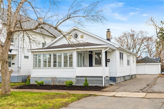 view of front of house featuring an outbuilding, a detached garage, covered porch, and a chimney