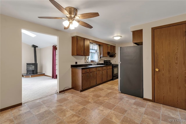 kitchen featuring a wood stove, freestanding refrigerator, under cabinet range hood, gas stove, and dark countertops