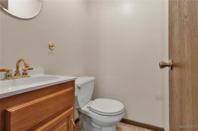 half bath featuring tile patterned floors, vanity, baseboards, and toilet