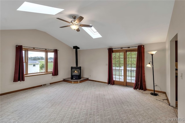 unfurnished living room with vaulted ceiling with skylight, a wood stove, ceiling fan, and carpet
