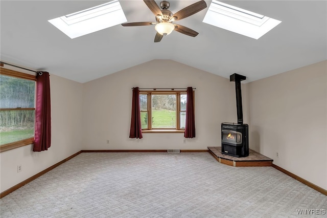 unfurnished living room featuring a wood stove, carpet, a ceiling fan, visible vents, and lofted ceiling with skylight