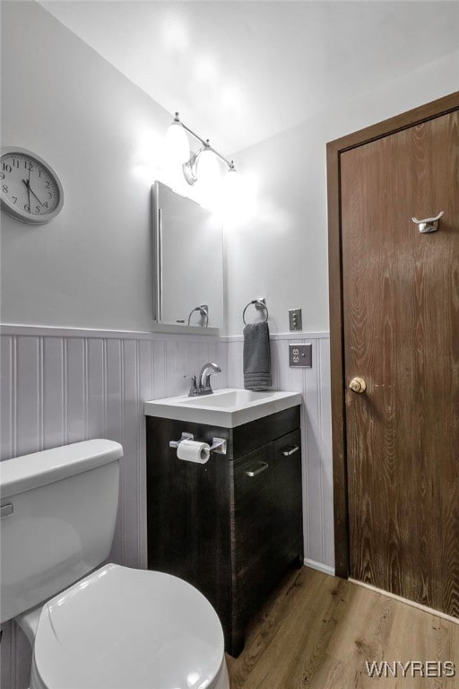 bathroom with toilet, wood finished floors, vanity, and wainscoting