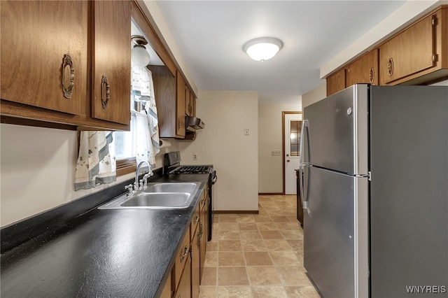 kitchen with a sink, dark countertops, under cabinet range hood, brown cabinetry, and stainless steel appliances