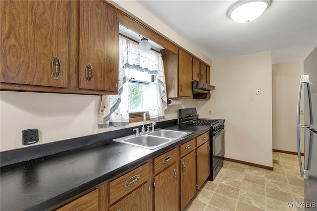 kitchen with brown cabinetry, under cabinet range hood, dark countertops, a sink, and black gas range oven