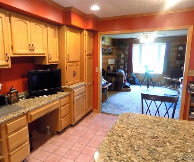 kitchen with light carpet, ceiling fan, built in study area, light tile patterned flooring, and crown molding