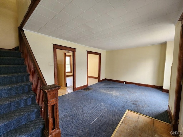 carpeted empty room with baseboards and stairway