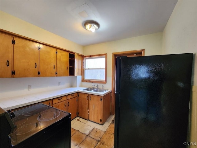 kitchen featuring black appliances, stone finish flooring, light countertops, a sink, and brown cabinets