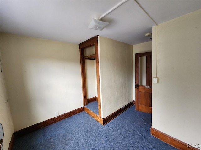 spare room featuring dark colored carpet and baseboards