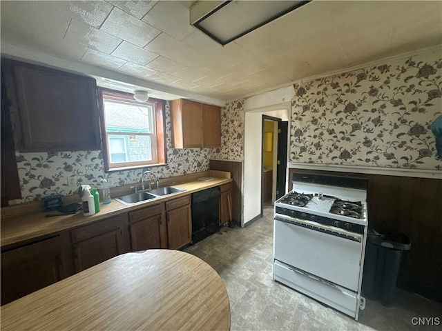 kitchen with white range with gas stovetop, black dishwasher, a sink, wainscoting, and wallpapered walls