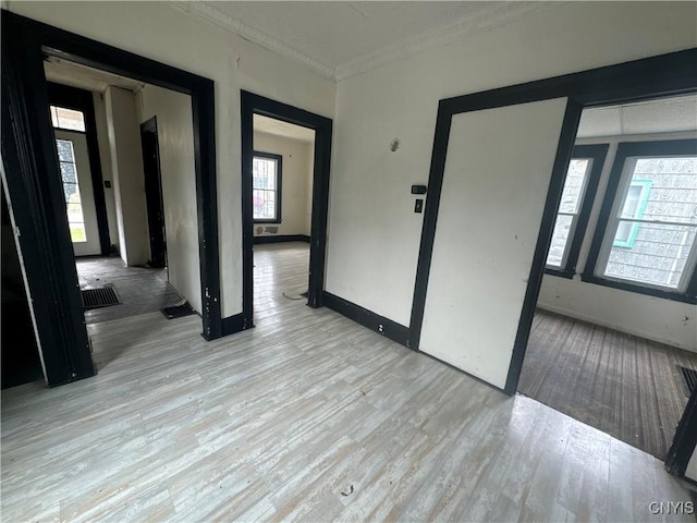 empty room featuring light wood-style flooring, baseboards, and ornamental molding