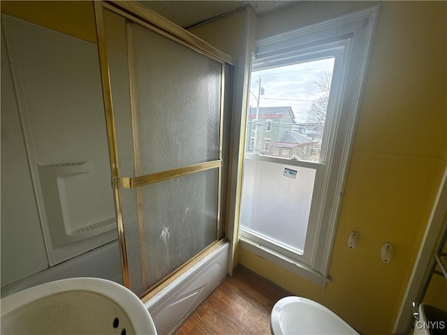 full bath featuring toilet, wood finished floors, and bath / shower combo with glass door