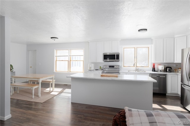 kitchen featuring a center island, a sink, light countertops, appliances with stainless steel finishes, and dark wood-style floors