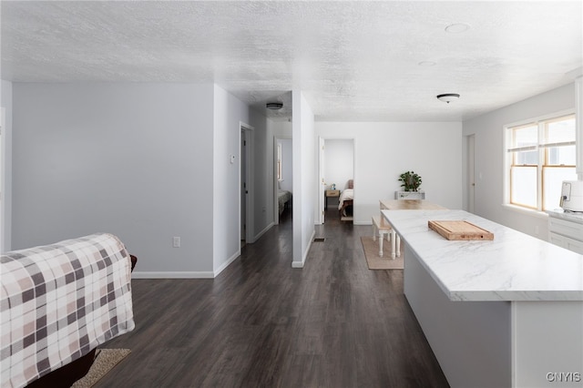 kitchen featuring dark wood-style flooring, baseboards, a kitchen island, and a textured ceiling