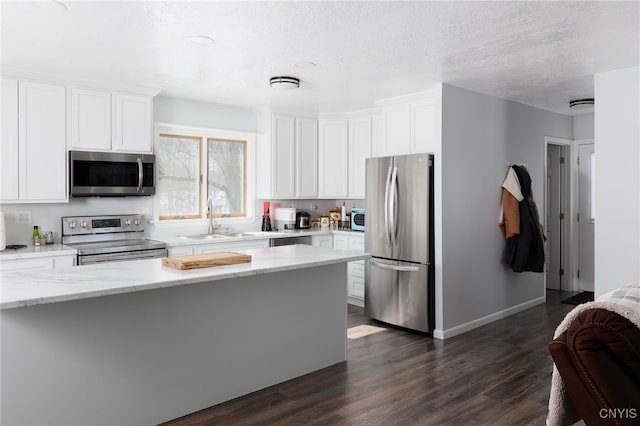 kitchen with appliances with stainless steel finishes, dark wood-style flooring, a sink, and white cabinetry