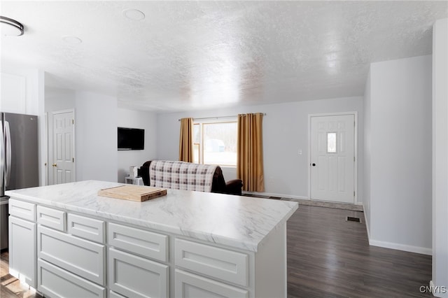 kitchen with open floor plan, white cabinetry, freestanding refrigerator, and a kitchen island