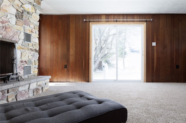 living area featuring visible vents, a stone fireplace, carpet, and wood walls