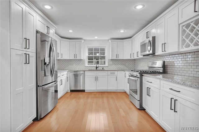 kitchen with backsplash, white cabinets, light wood-style floors, stainless steel appliances, and a sink