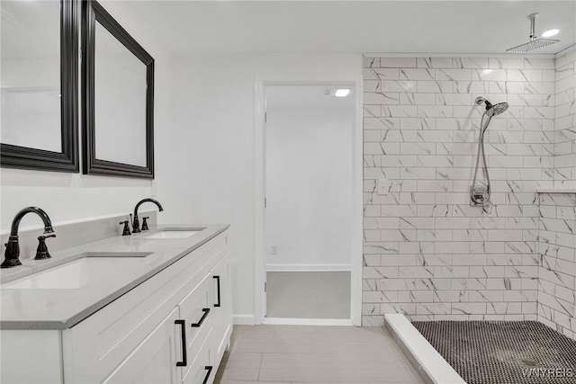 full bath featuring a shower stall, double vanity, a sink, and baseboards