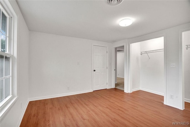 unfurnished bedroom with wood finished floors, baseboards, a closet, and a spacious closet