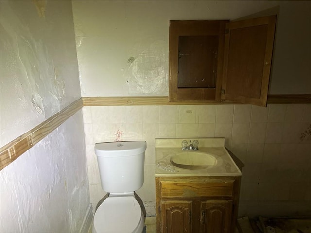 bathroom with a textured wall, vanity, tile walls, and toilet