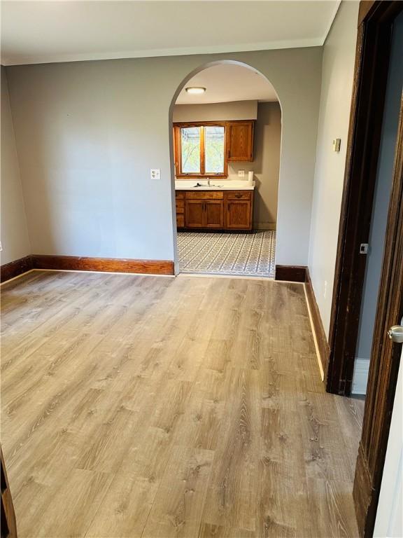 spare room featuring baseboards, light wood finished floors, and arched walkways