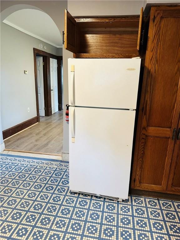 kitchen with baseboards, ornamental molding, freestanding refrigerator, light wood-style floors, and arched walkways