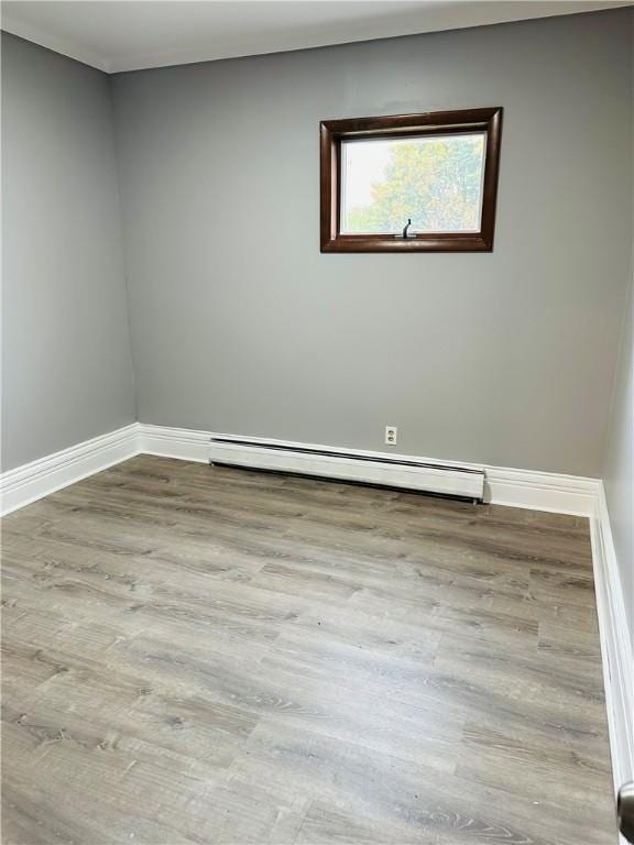 empty room featuring a baseboard heating unit, baseboards, and wood finished floors