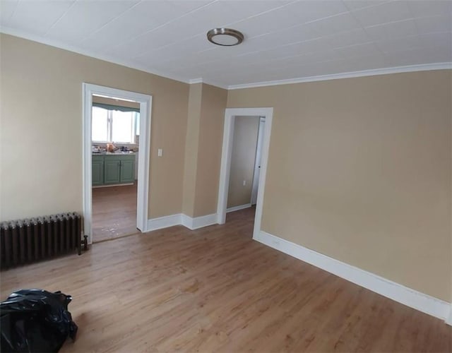 spare room featuring ornamental molding, radiator heating unit, light wood-style floors, and baseboards