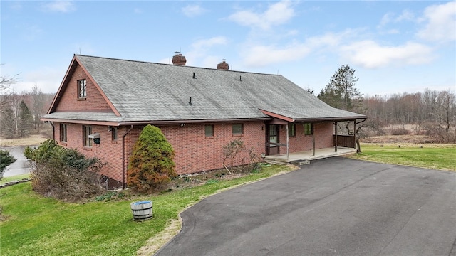 rear view of house featuring a porch, brick siding, a chimney, and a lawn