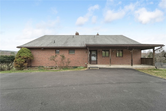 rear view of house with roof with shingles, aphalt driveway, brick siding, and a chimney
