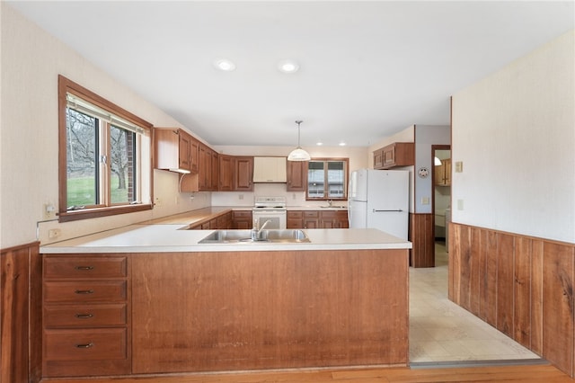 kitchen with a sink, white appliances, a peninsula, wooden walls, and wainscoting