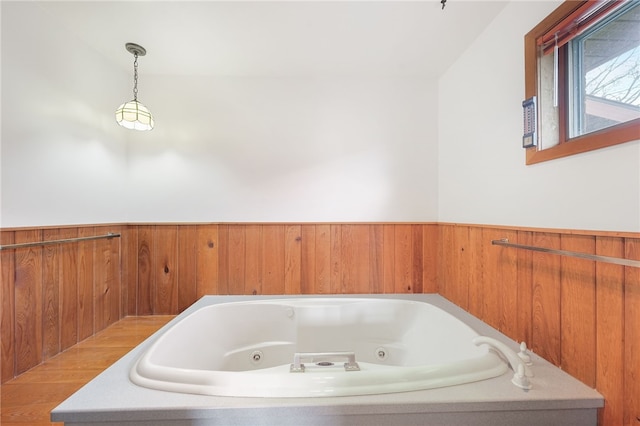 bathroom with wood walls, a whirlpool tub, and a wainscoted wall