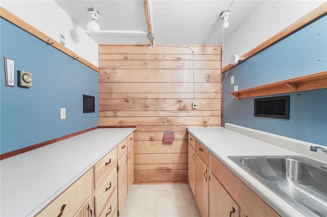 kitchen featuring visible vents, light brown cabinets, a sink, light countertops, and wooden walls